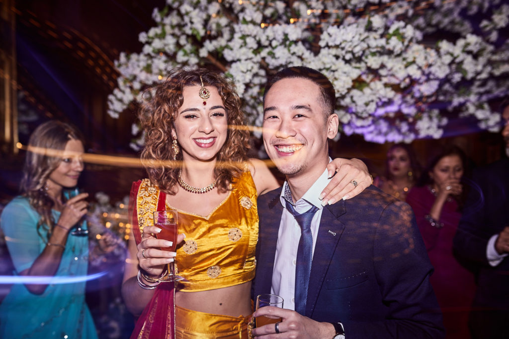 Two wedding guests smiling with drinks on the dance floor under blossom trees