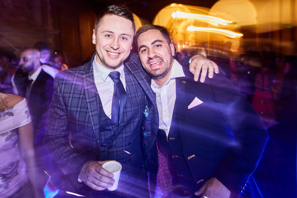 Two guests in suits posing arm in arm on the dance floor