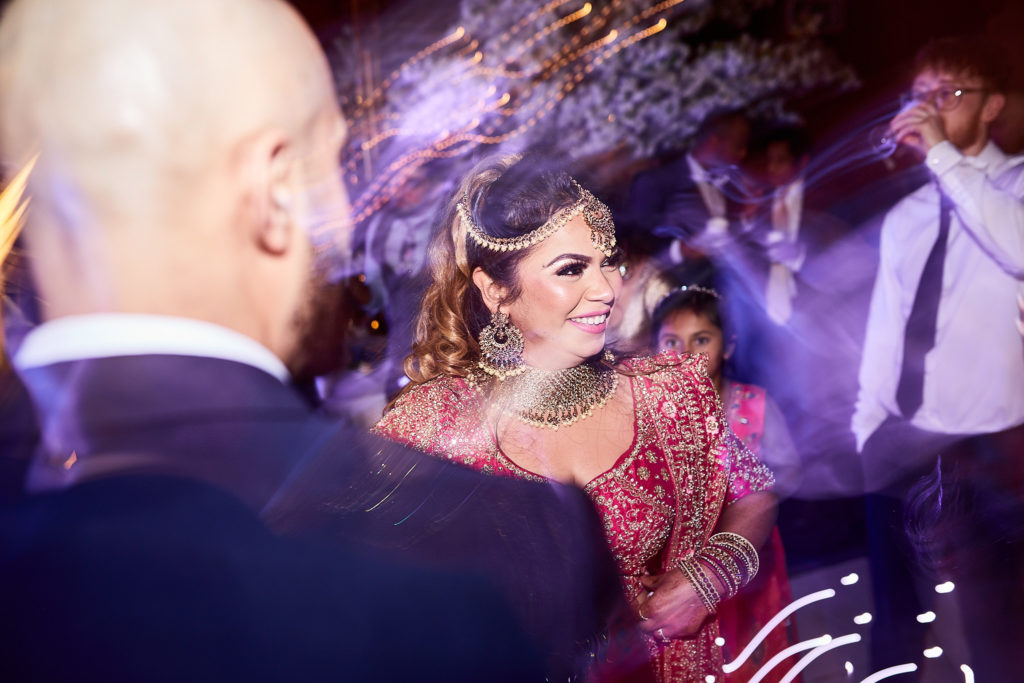 Bride in her red lehenga and jewellery dancing with the groom