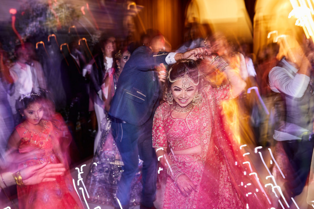 Bride dancing in a pink lehenga surrounded by guests