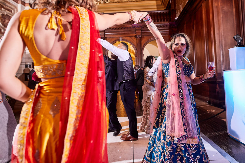 Bridesmaids in colourful lehengas dancing in the wood-panelled hall
