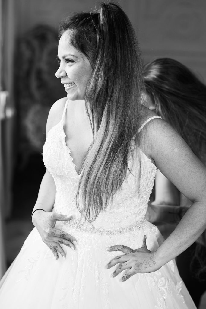 Black and white photo of the bride laughing as she gets into her wedding dress