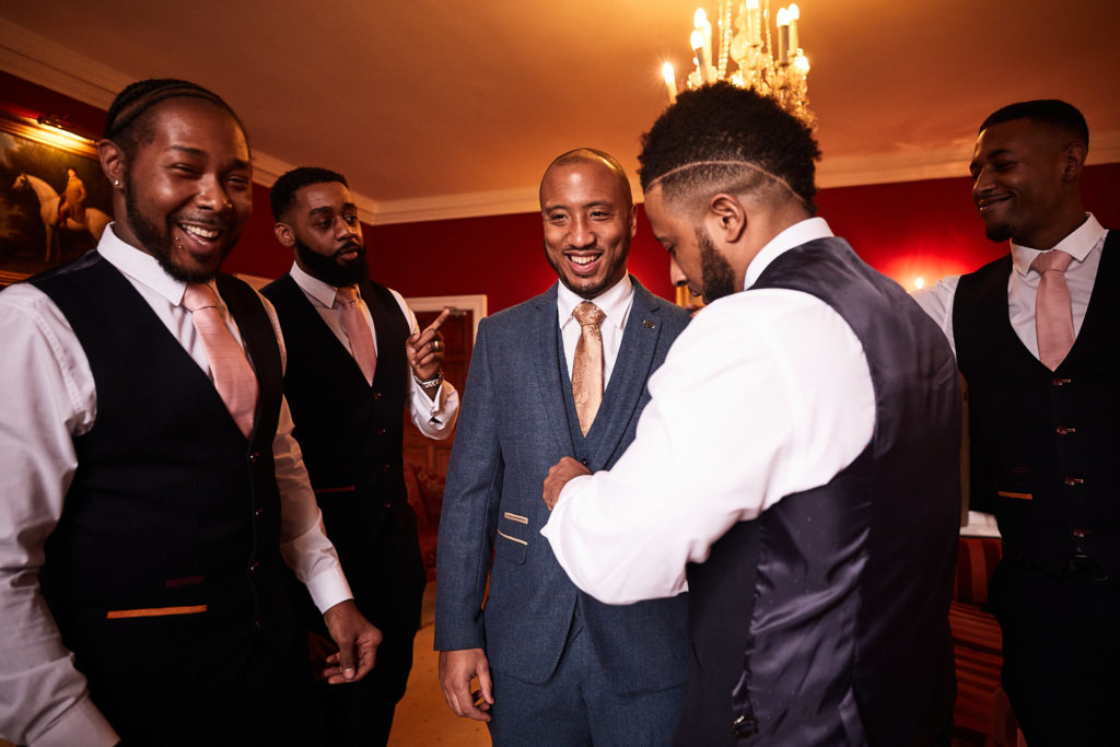 Groomsmen helping the groom get ready under a chandelier