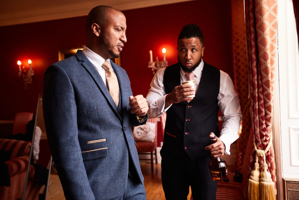 Groom and a groomsman chatting in a red-walled room at Addington Palace