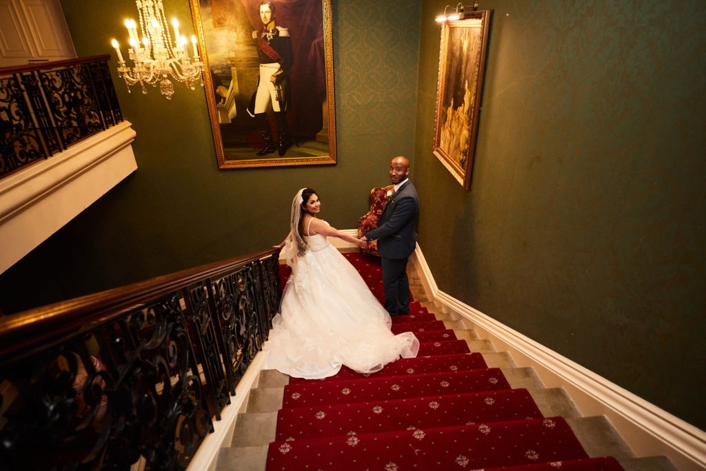 Bride and groom on the red-carpeted grand staircase at Addington Palace
