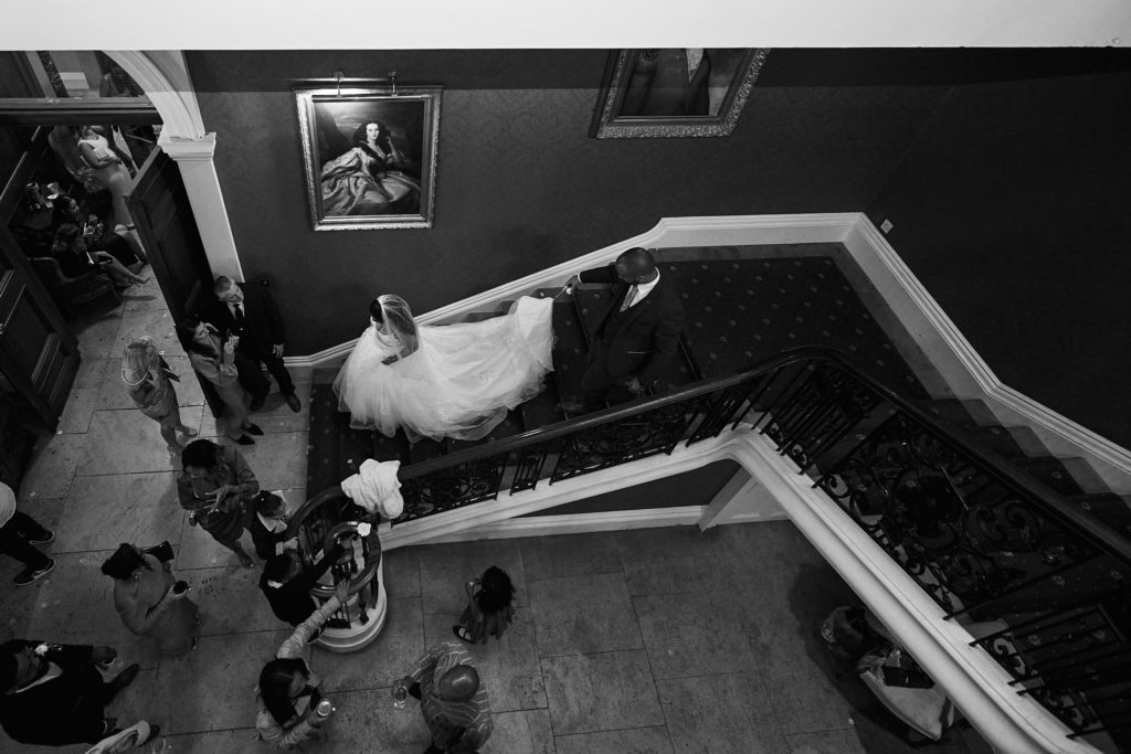 Black and white photo from above of the bride and groom on the grand staircase at Addington Palace