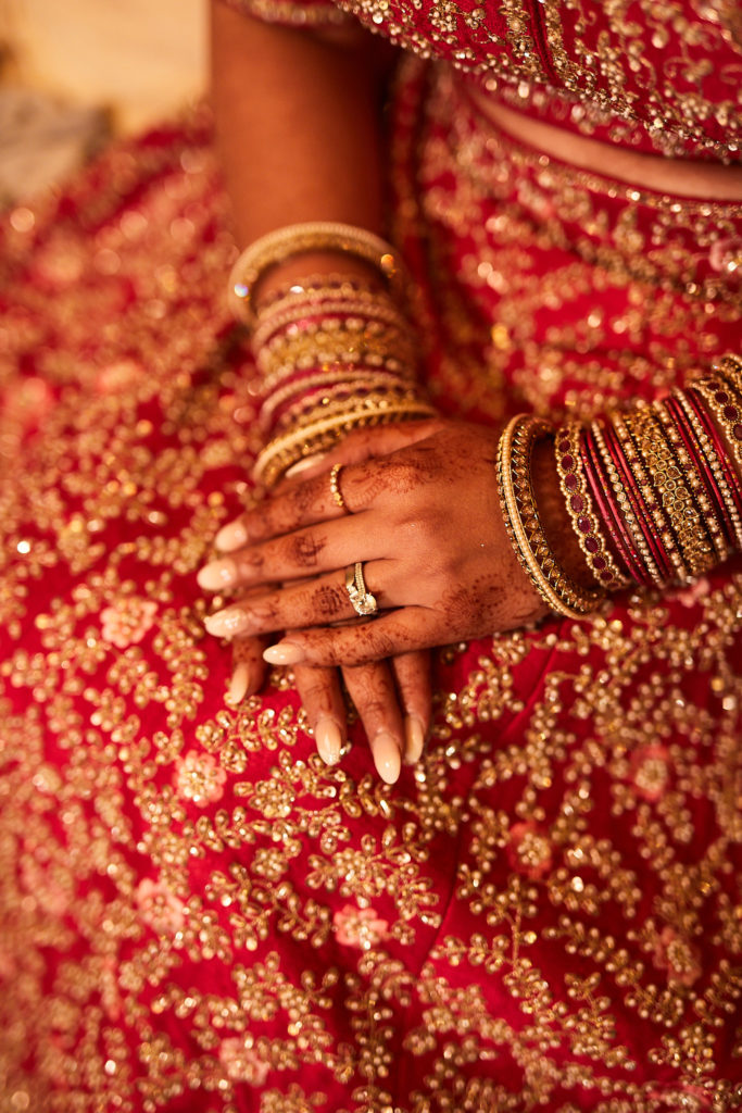 Close-up of the bride's hennaed hands, bangles and ring against her red lehenga