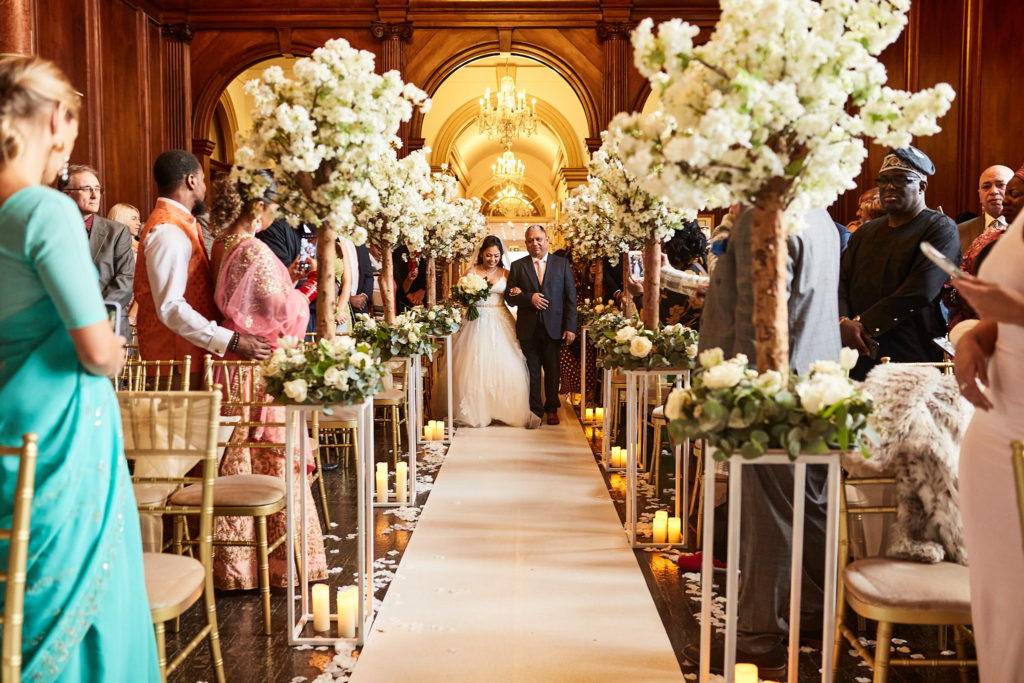 Bridesmaid walking down the aisle between blossom trees as guests watch