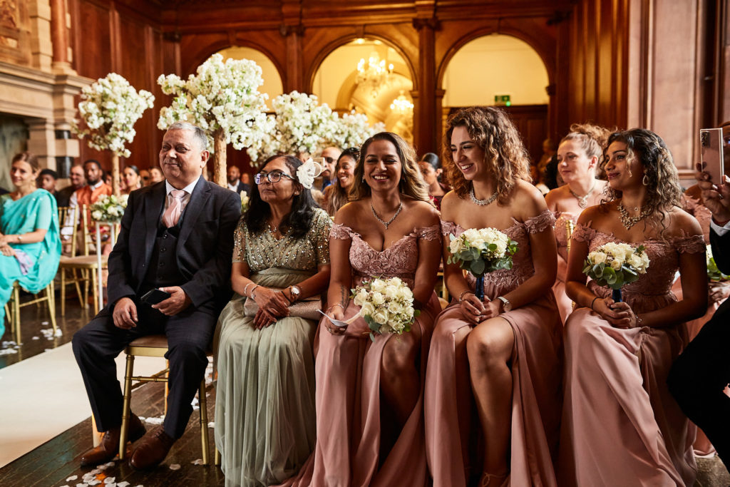 Bridesmaids in blush pink dresses seated in the front row with their bouquets