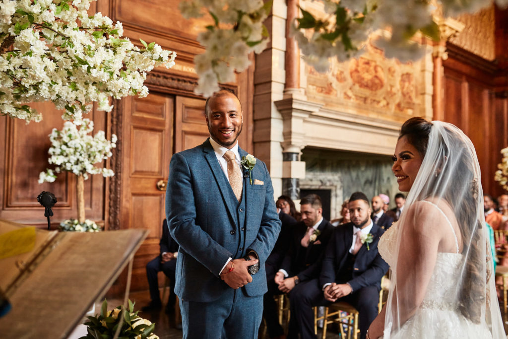 Groom smiling at the bride at the front of the ceremony at Addington Palace