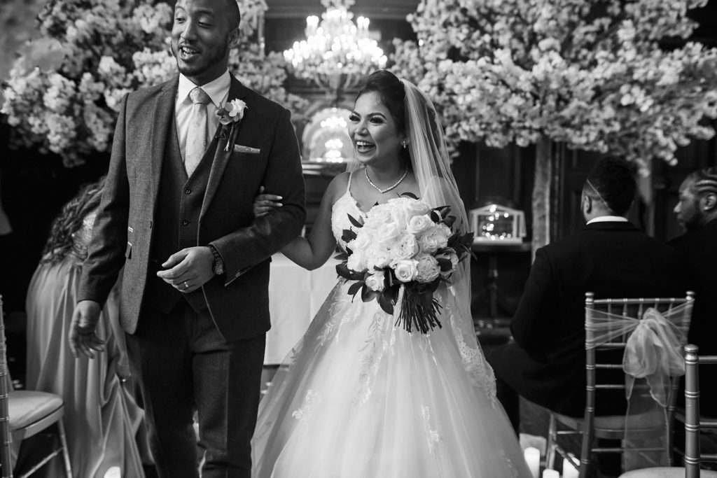 Black and white photo of the bride and groom walking back down the aisle under blossom trees