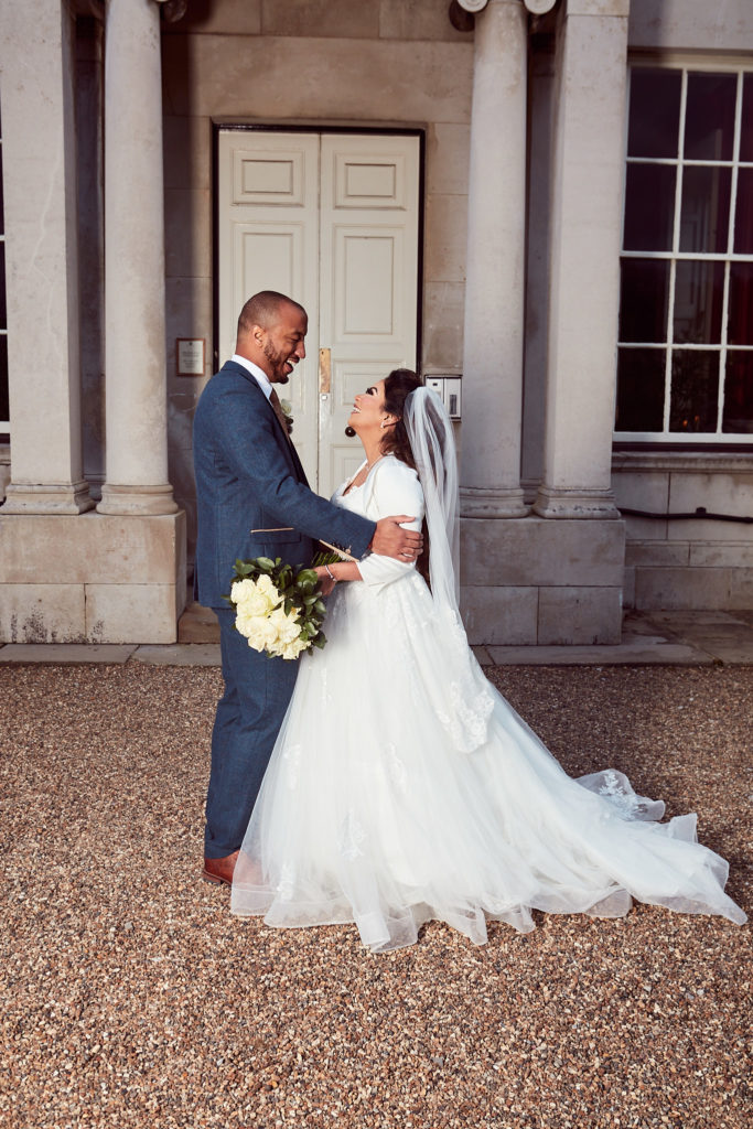 Bride and groom laughing together in front of the columns at Addington Palace