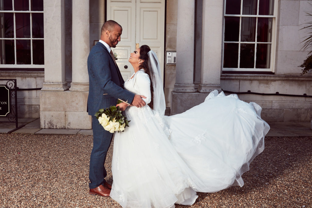 Bride and groom embracing as her dress swirls outside Addington Palace