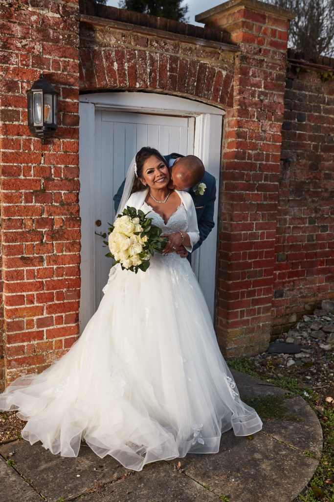Groom kissing the bride's cheek in a brick doorway at Addington Palace