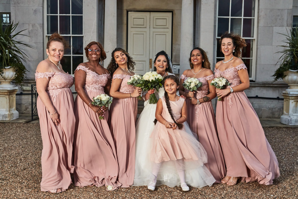 Bride with her bridesmaids in blush pink dresses and a flower girl outside Addington Palace