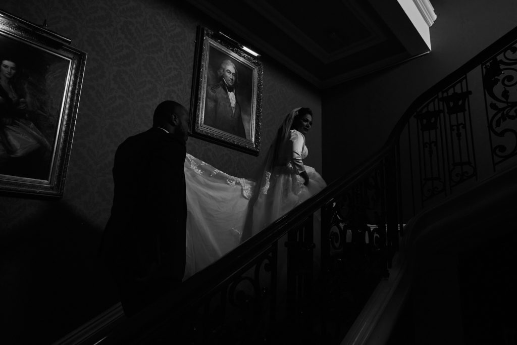 Bride and groom on the dimly lit grand staircase at Addington Palace