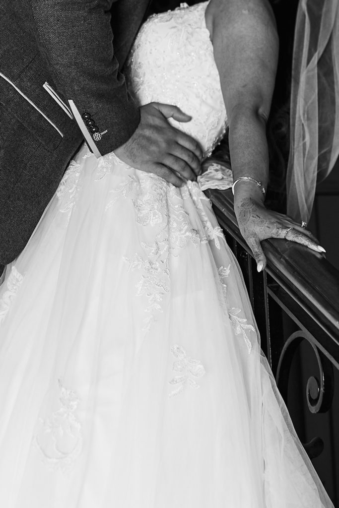 Black and white close-up of the groom's hand on the bride's waist on the staircase