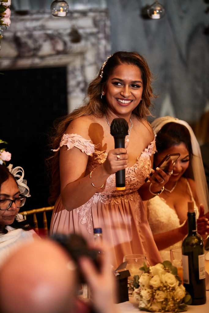 Bridesmaid in a blush pink dress giving a speech with a microphone