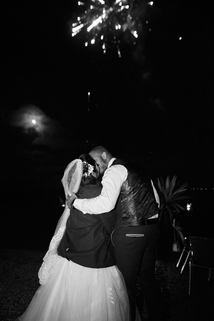 Black and white photo of the bride and groom kissing under fireworks at Addington Palace