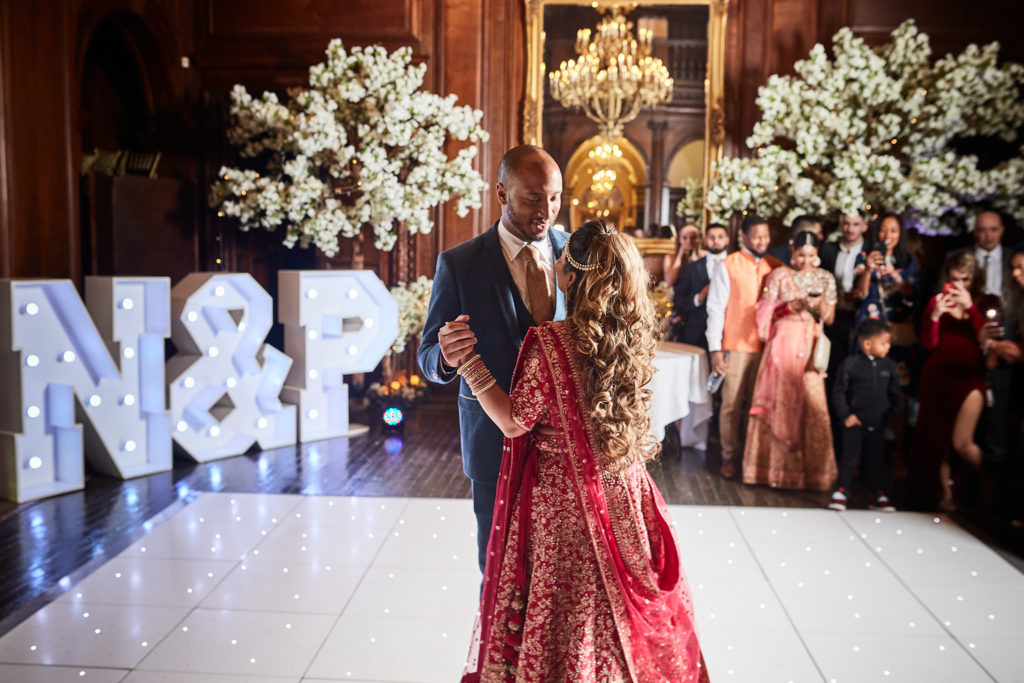 Bride in a red lehenga dancing with the groom in front of illuminated N and P letters