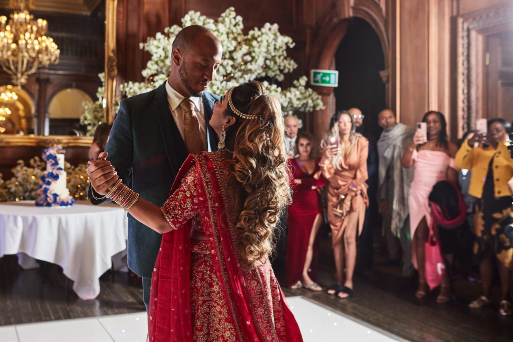 Bride in a red lehenga and the groom on the dance floor as guests watch