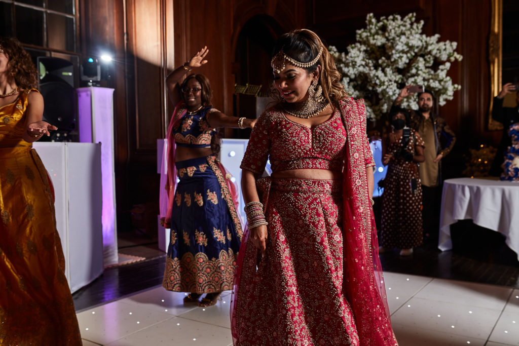 Bride in a red and gold lehenga on the dance floor at Addington Palace