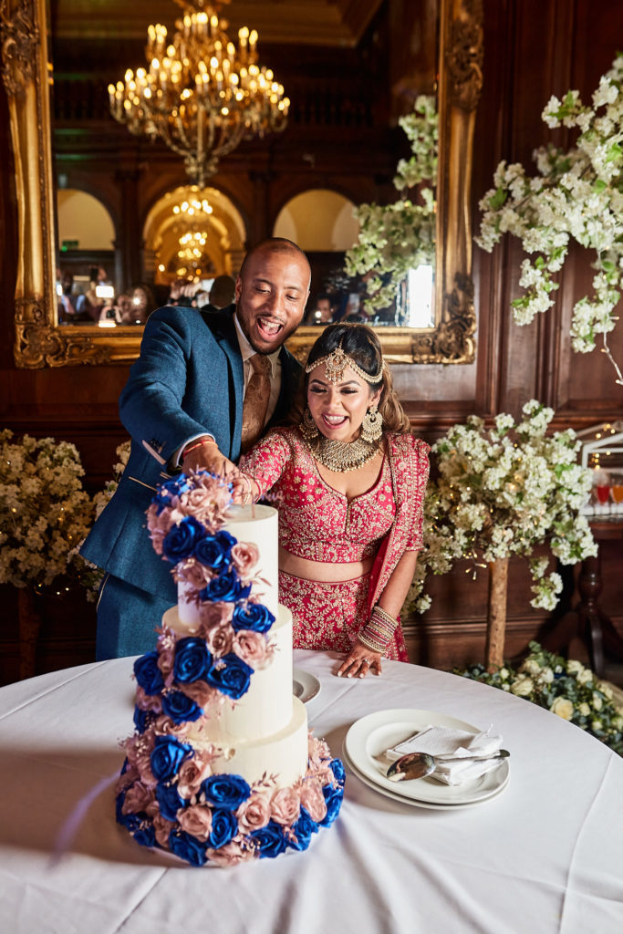 Bride and groom laughing as they cut their rose-covered wedding cake