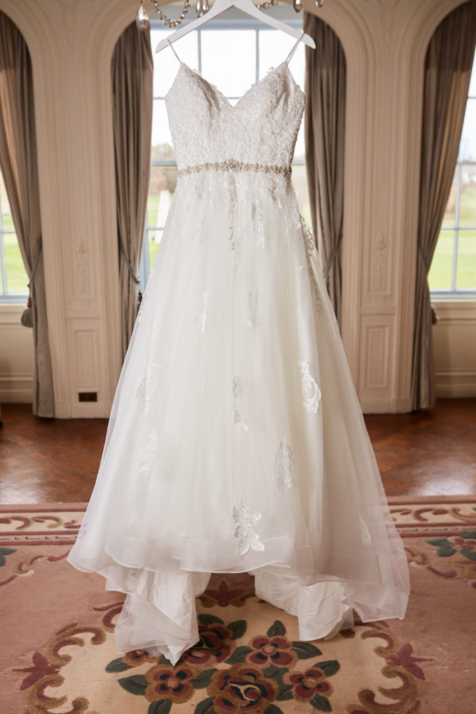 Lace wedding dress with a beaded belt hanging in the bridal suite at Addington Palace