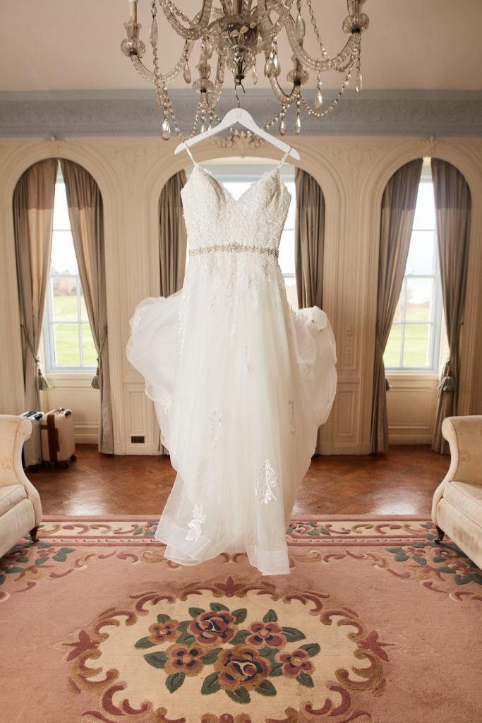Wedding dress hanging from a chandelier between tall arched windows