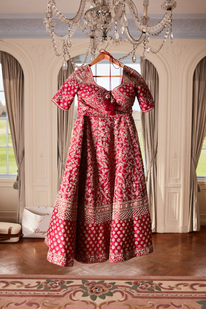 Red and gold bridal lehenga hanging from a chandelier in the bridal suite