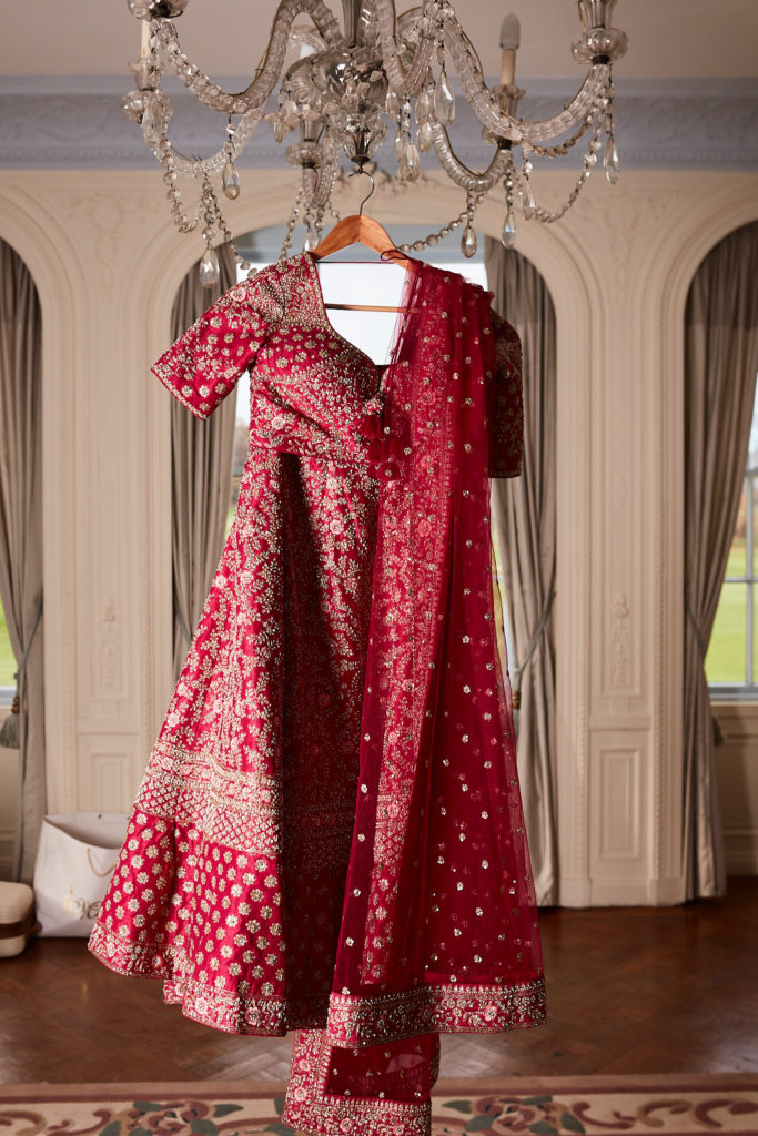Red bridal lehenga and embroidered dupatta hanging from a chandelier