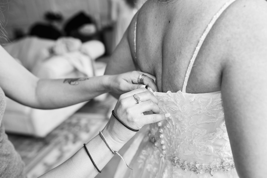 Black and white close-up of the back of the bride's dress being fastened