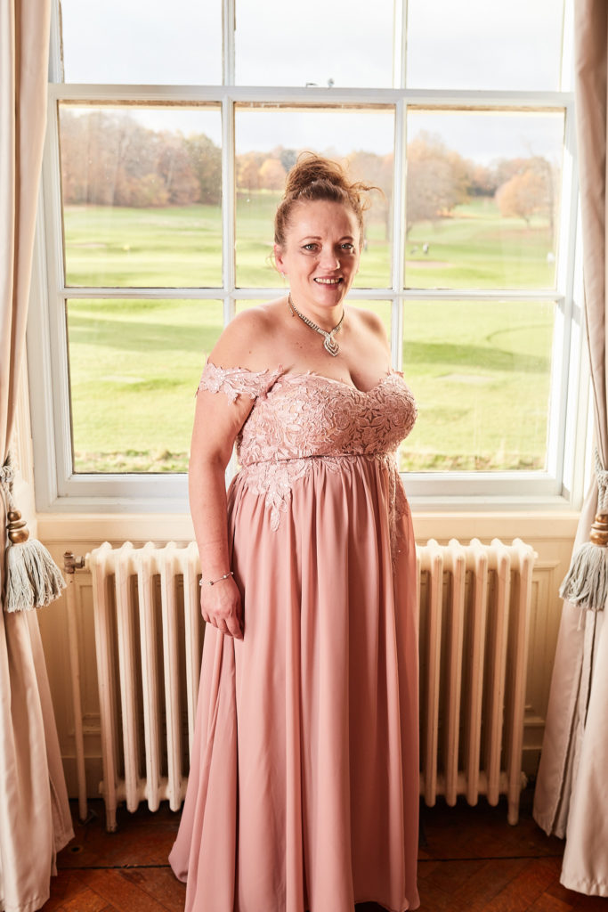 Bridesmaid in a blush pink lace dress in front of a window