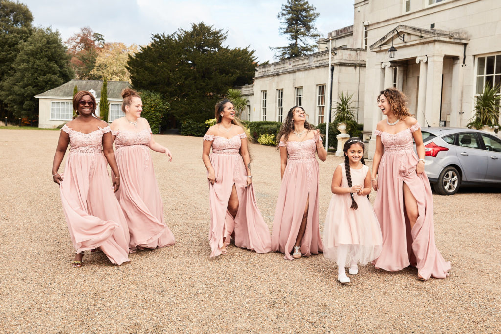 Bridesmaids and a flower girl laughing as they walk in front of Addington Palace