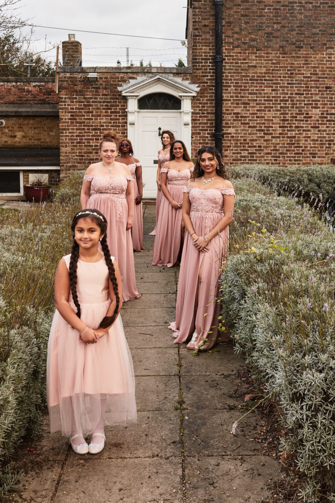 Flower girl and bridesmaids in blush pink lined up along a garden path