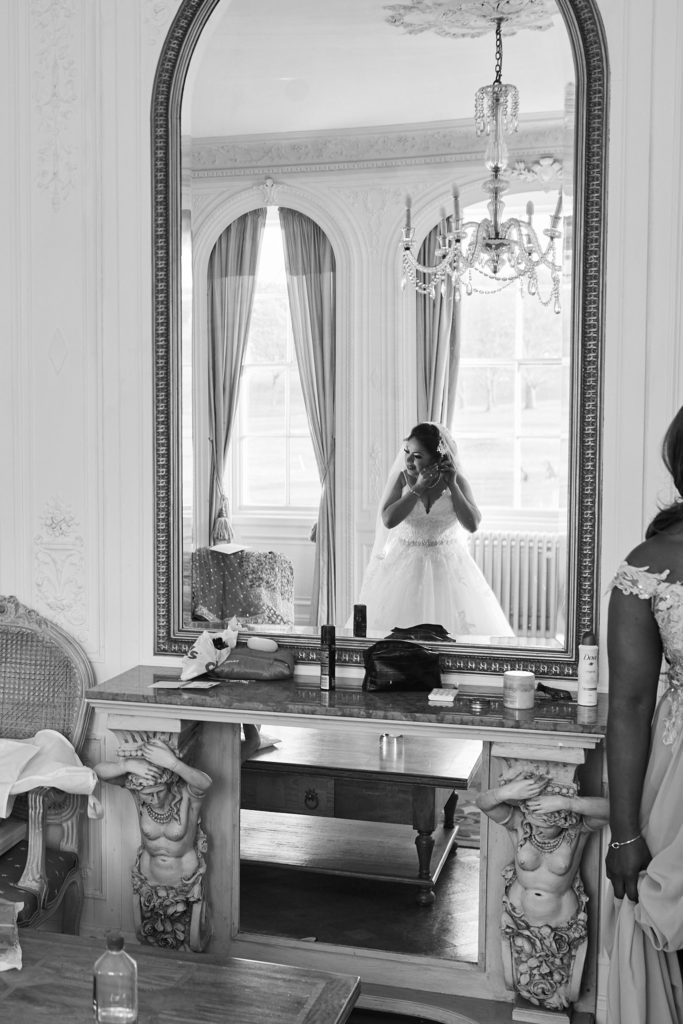 Black and white photo of the bride in her wedding dress reflected in a large mirror