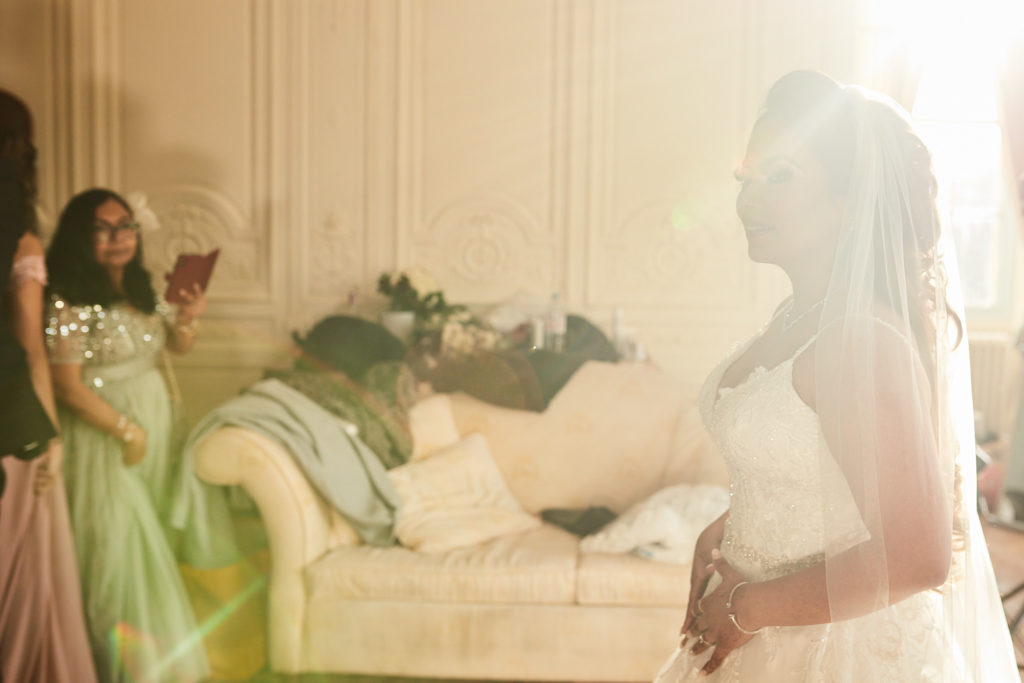 Bride in her wedding dress in soft window light with a bridesmaid behind