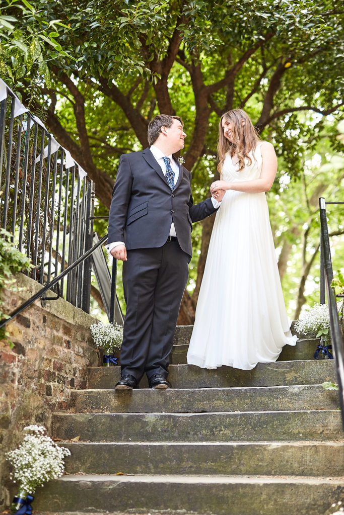 Bride and groom laughing together on stone steps under the trees
