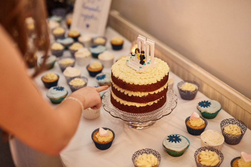 Naked wedding cake surrounded by cupcakes as a guest helps herself