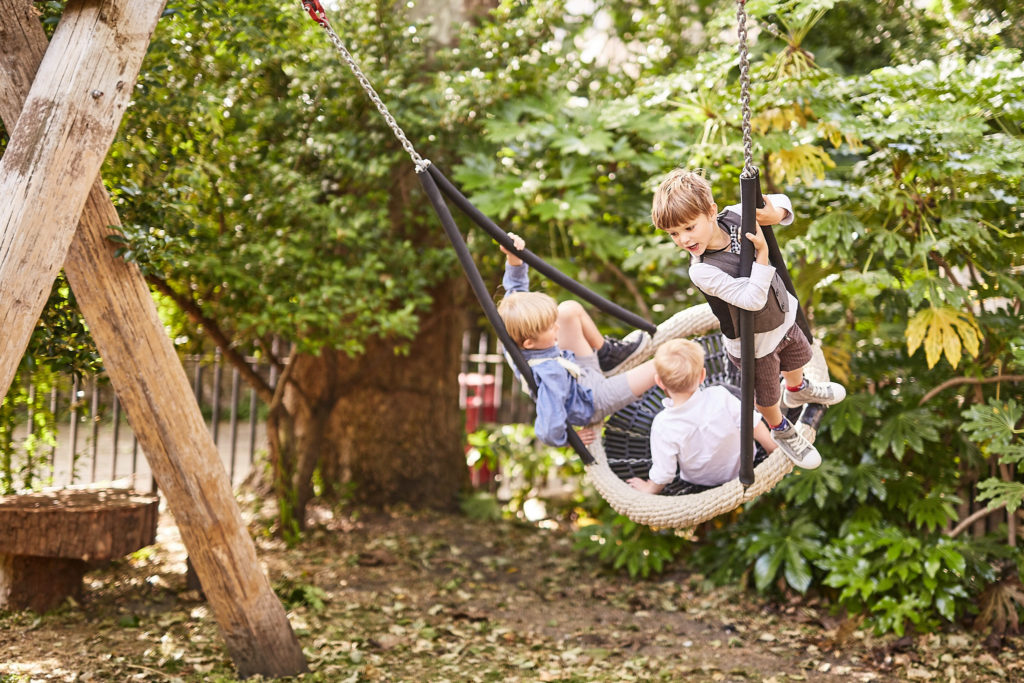 Children playing on a hammock swing under the trees
