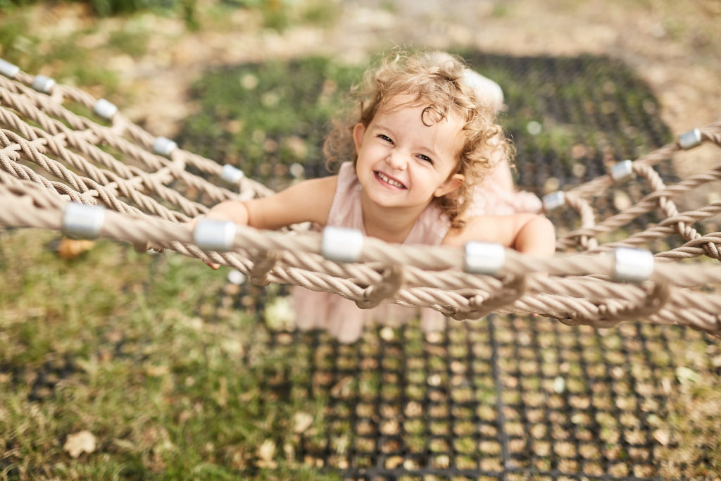 Toddler smiling as she lies on a rope hammock