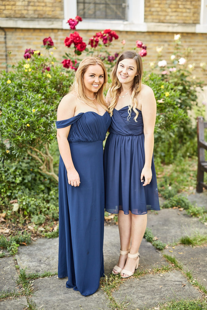 Two bridesmaids in navy dresses standing in front of a rose bush