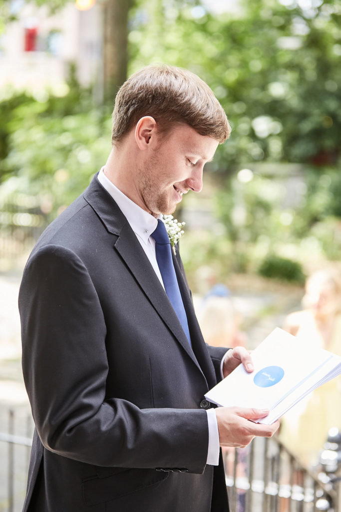 Man in a navy suit reading the order of service outdoors