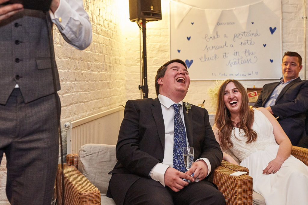 Bride and groom laughing on a sofa during the speeches