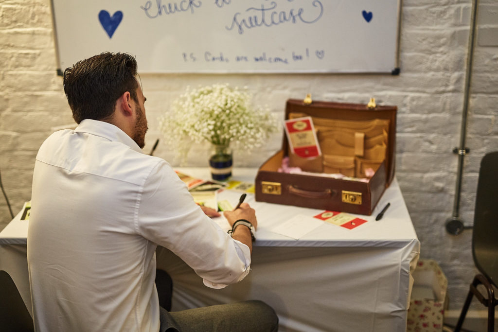 Guest writing a message beside a vintage suitcase guest book