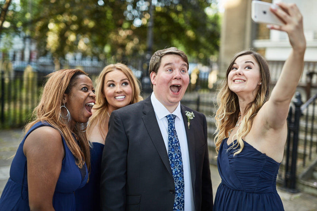 Groom pulling a face as he takes a selfie with the bridesmaids
