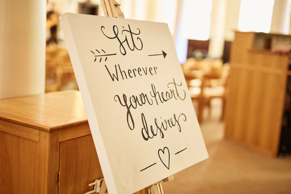 Handwritten "Sit wherever your heart desires" sign on an easel in the church
