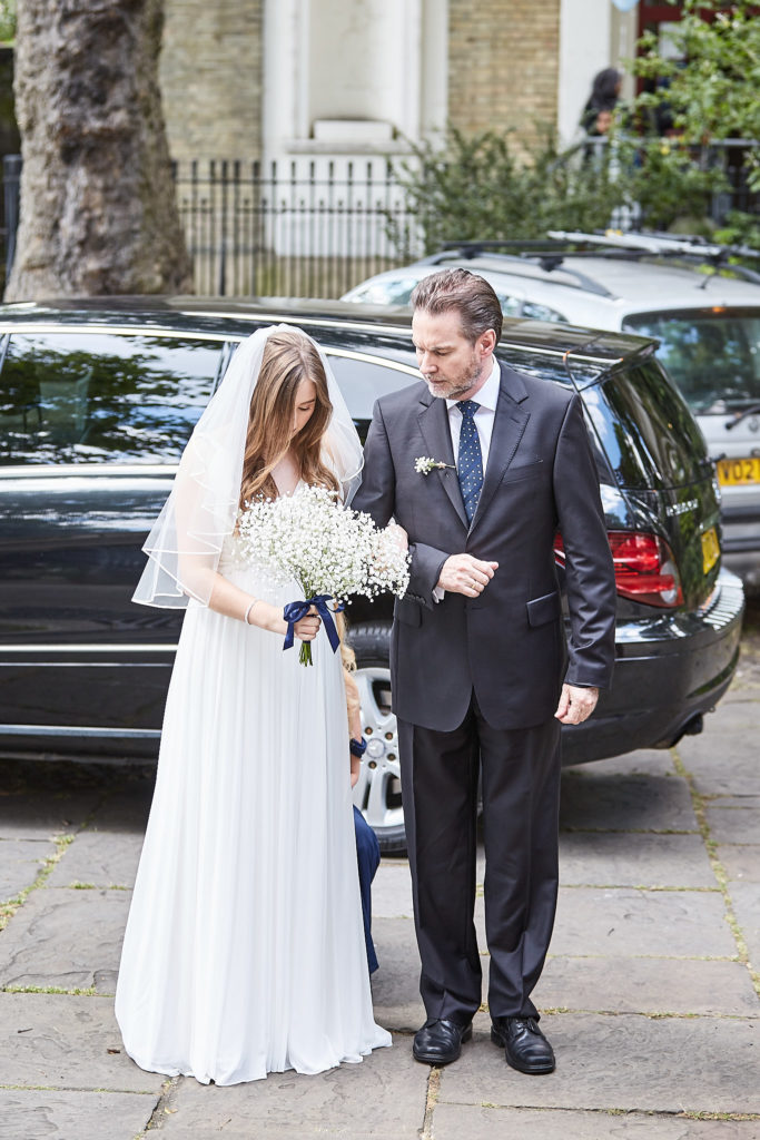 Bride in her veil arriving at the church on the arm of a man in a dark suit
