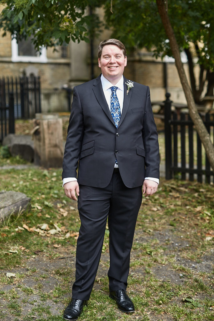 Groom smiling in a navy suit in the churchyard
