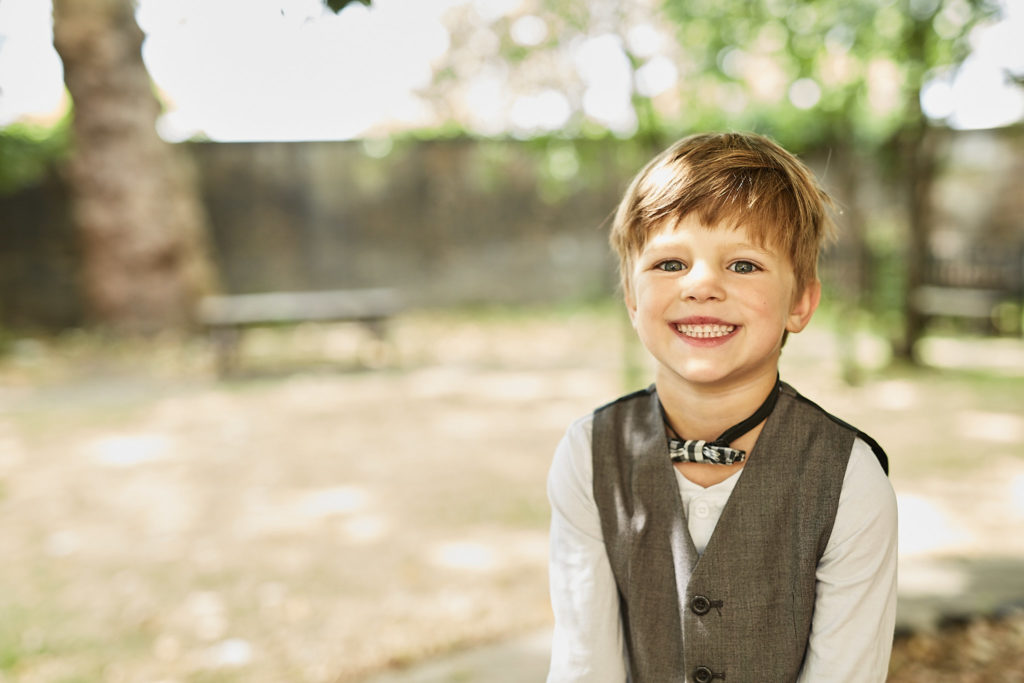 Young page boy in a waistcoat smiling in the churchyard